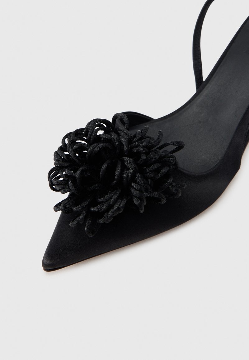 Sort satinpumps med spids tå, der har en struktureret blomst detalje af snoet sort stof på overdelen. Åben bagdesign.