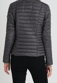 Giacca grigia imbottita con un design trapuntato, spalle arrotondate e toppe sui gomiti. Presenta un colletto alto e una silhuette aderente.