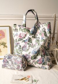 Gėlėmis dekoruota rankinė su rožinėmis, mėlynomis ir žaliomis gėlėmis ant baltos medžiagos. Pridedama mažesnė, deranti užtrauktuko kišenė.