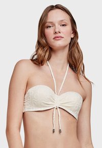 Strapless crèmekleurige bikini-top met een gestructureerd spiraalpatroon, een verzameld midden en verstelbare bandjes. Kenmerkt metalen accenten op de uiteinden van de bandjes.