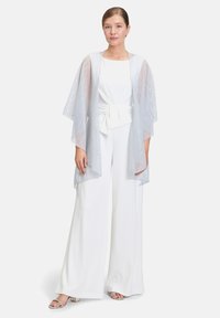 Kimono en argent léger et transparent avec un motif texturé. Porté sur une combinaison blanche avec une taille nouée et des jambes larges.