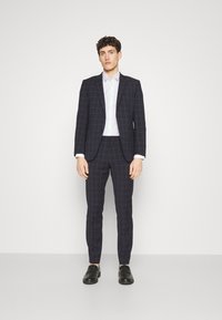 Navy checked suit with slim fit, paired with a white button-up shirt. Black leather shoes complete the outfit, highlighting tailored details.