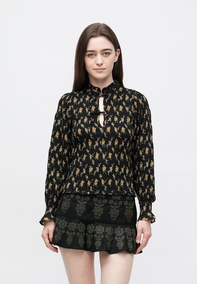 Black floral blouse with a smocked texture, featuring a keyhole opening and long sleeves. Paired with a tiered black skirt with green embroidery.