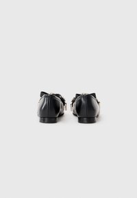 Black leather flats with a rounded toe and small low heel. Features metallic accents and a decorative strap at the back. Smooth texture.