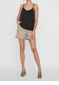 Top nero senza maniche con un design arricciato, abbinato a pantaloni corti khaki. Il modello indossa mule con tacco a fantasia serpentina.
