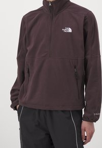 Maglione in pile bordeaux con collo alto, chiusura a mezza zip, due tasche con zip e logo "The North Face" ricamato sul petto.