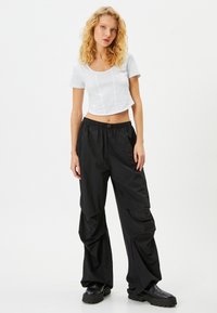 Hvid cropped top med korte ærmer, parret med sorte, løse cargo-bukser med en sammenkrøllet talje og tekstureret stof.