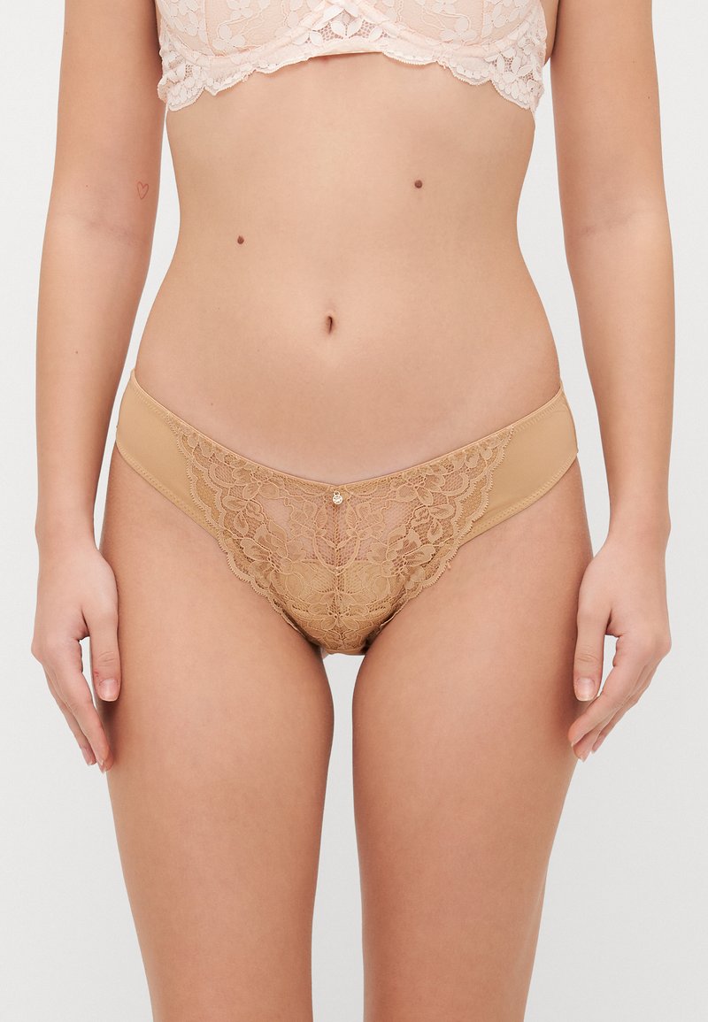 Lenjerie din dantelă într-o nuanță nud, cu modele florale, având un front din plasă, părți laterale netede și un mic accent decorativ în centru.