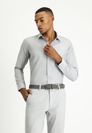 Camisa de botones de manga larga gris claro con un sutil patrón de rayas. Combinada con pantalones gris claro y un cinturón tejido gris.