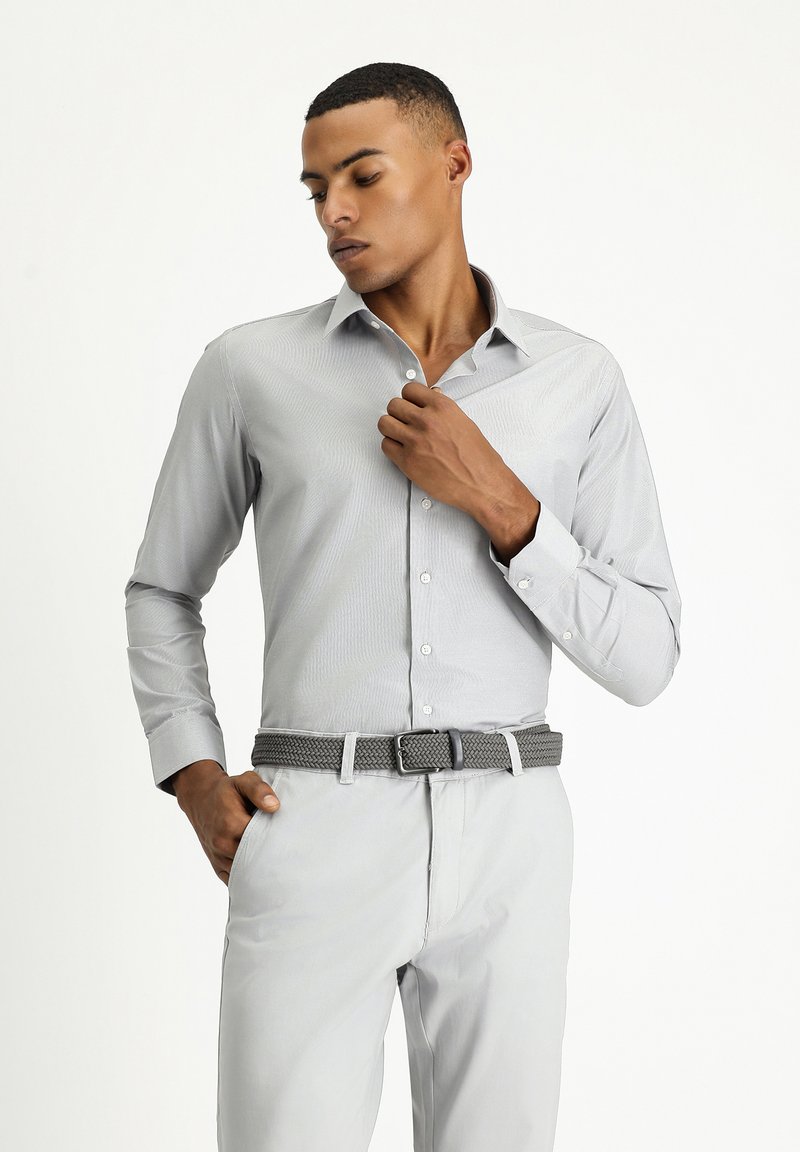 Lichtgrijze, lange mouwen overhemd met een subtiel streeppatroon. Gecombineerd met lichtgrijze broek en een geweven grijze riem.