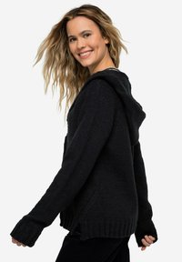 Felpa nera a maglia con un fit rilassato, polsini e orlo a coste. Presenta una texture morbida e un cappuccio per maggiore calore.