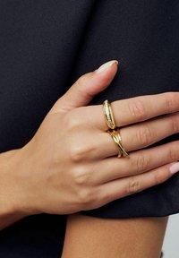 To goldringe på en hånd, den ene glat og rund, den anden med et snoet design. Hånden mod en mørk stofbaggrund.