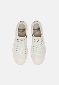 Paire de baskets basses blanches Palladium avec lacets à l'avant, semelles texturées et semelles intérieures de marque, vue de dessus sur un fond uni.