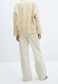 Veste beige texturée à coupe décontractée avec une taille élastiquée, associée à un pantalon cargo crème taille haute avec poches latérales.