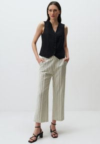 Gilet en lin noir avec un col en V et six boutons, associé à un pantalon à jambes larges rayé blanc. Des sandales à talons noires à brides complètent l'ensemble.