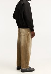 Svart bombarjacka, beige vida jeans med en blek textur och grå sneakers. Jackan har elastiska ärmslut och midja.