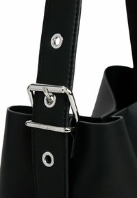 Zwarte nep leren handtas met een zilveren gesp en oogjesdetail op de schouderband. Bevat een zachte, gestructureerde ontwerp en het merklogo.