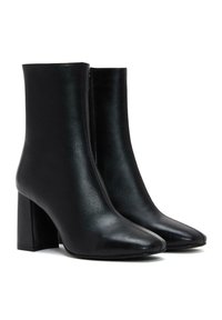 Bottines en cuir noir avec un bout pointu et un haut talon carré, présentant un design sans couture et une fermeture éclair à l'arrière.
