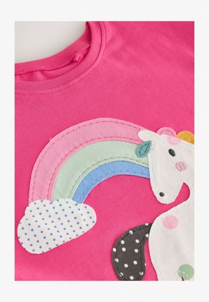 Rózsaszín pamut ing, amelyen applikált unikornis minta látható, szivárvánnyal. A szivárvány pasztellszínekből áll; a felhő fehér, kék pöttyökkel díszítve.