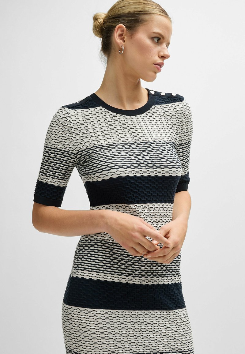 Strickkleid mit taillierter Silhouette, ausgestattet mit navy- und cremefarbenen horizontalen Streifen, strukturierten Wellenmustern und dekorativen Knöpfen an der Schulter.