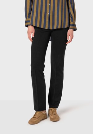 Zwarte, rechte broek van een zachte, gestructureerde stof, gecombineerd met een gestreept overhemd met knopen en beige suède sneakers.