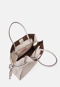 Ljust grå läderhandväska med en brun inredning. Har dubbla handtag, ett ficka med dragkedja och en knutdetalj på ena sidan.