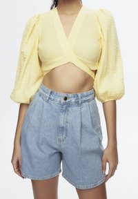 Haut court jaune texturé avec manches bouffantes, associé à un short en denim bleu taille haute. Le haut présente un design croisé et une silhouette ajustée.