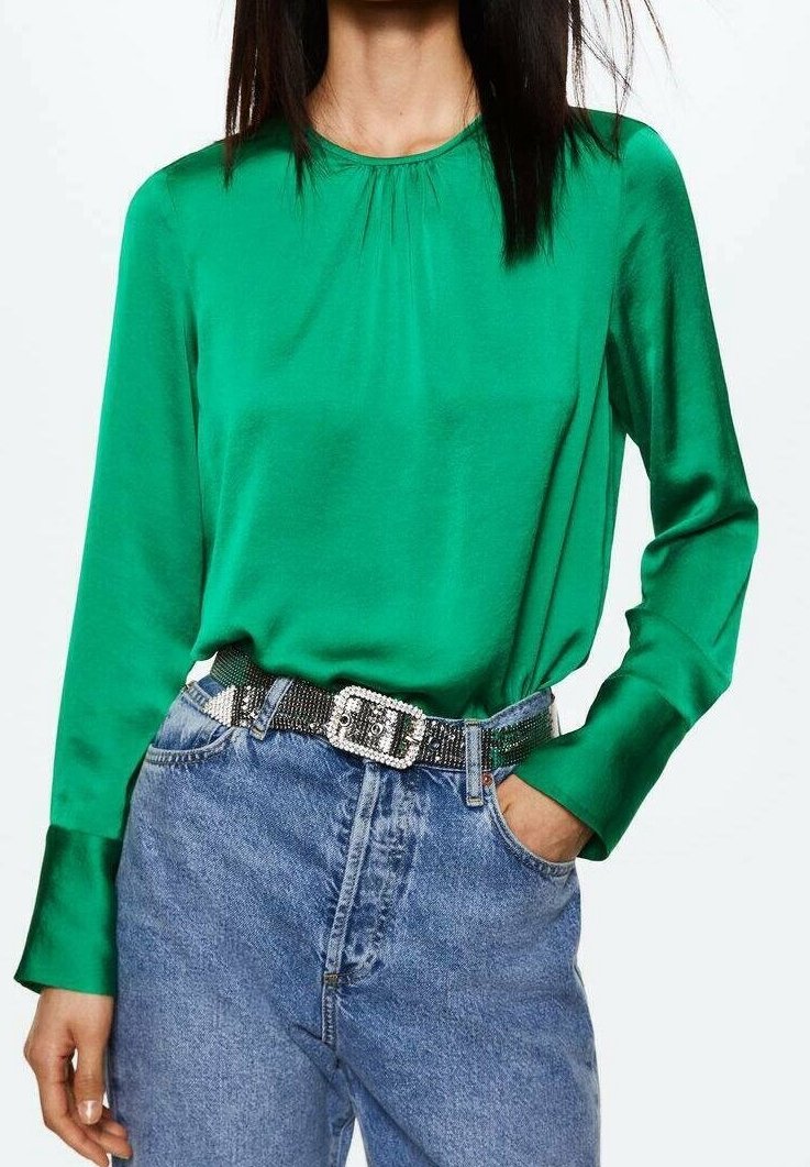 Femme portant un chemisier vert brillant à manches longues, rentré dans un jean bleu taille haute avec une ceinture noire dotée d'une grande boucle carrée.