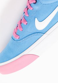Blå canvas sneakers med rosa snören, med en vit swoosh-logotyp och en strukturerad rosa gummisula. Kurvad form med stickade detaljer.