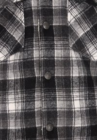 Zwart-wit geruite shirt van textuurstof, met contrasterende vierkanten, twee metalen knopen en een kraagdetails.