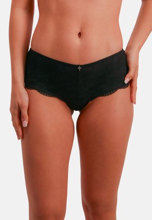 Shorty garçon en dentelle noire avec bords festonnés, orné d'un accent métallique décoratif à l'avant. Texture douce avec une coupe ajustée.