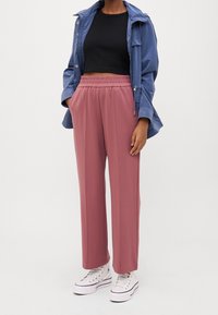 Lehká modrá bunda, černý top na crop a růžové široké kalhoty s elastickým pasem. Bílé tenisky s černými akcenty dotvářejí celkový vzhled.