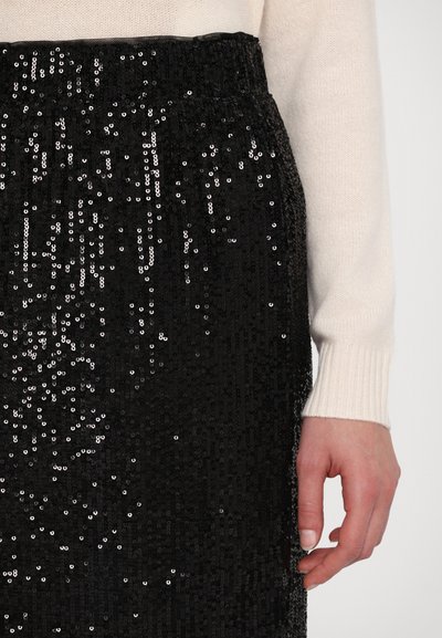 Sort pailette nederdel med elastisk talje, der har en blank finish og en struktureret stof. En hånd er delvist synlig, iført en lysfarvet sweater.