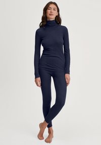 Marineblauwe lange mouwen coltrui gecombineerd met bijpassende leggings. Zachte stof met een gladde textuur en een figuurvormend design.