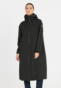 Zwarte lange jas met een rits aan de voorkant, capuchon en lange mouwen. Gemaakt van een soepele stof, met een logo-accent op de linker schouder.