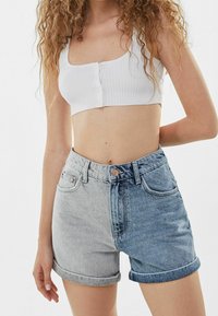 Vahvahihaiset denimshortsit, joissa on korkea vyötärö ja jaettu vaalea harmaa ja sininen kuvio. Shortseissa on kääritty reunat ja napillinen vetoketjusulku.