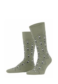 Olivgrüne Socken mit einem Rautenmuster in Marineblau und Weiß, die kleine Bleistiftzeichnungen zeigen. Stricktextur mit einem gerippten Bund.