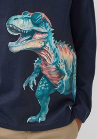 Navyblaues Hemd mit einem bunten Dinosaurier-Design, der Sonnenbrille und ein Hemd trägt, mit detaillierten Schuppen und Verzierungen auf seinem Körper.