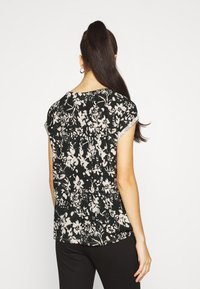 Černý top s květinovým potiskem, krátkými rukávy, kulatým výstřihem, vyrobený z měkké látky, s bílými květinovými vzory a volnějším střihem.