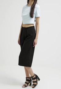 Light blue cropped top with a decorative neckline, paired with high-waisted black wide-leg trousers and strappy black heeled sandals.
