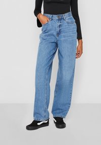 High-waisted blue denim jeans with a relaxed fit, featuring front pockets and a button closure. Worn with black sneakers.