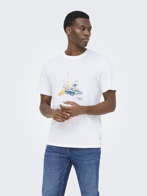 Νέος άνδρας φοράει λευκό t-shirt με πολύχρωμο σχέδιο vintage αυτοκινήτου και παρισινών αξιοθέατων, συνδυασμένο με μπλε τζιν, στέκεται μπροστά σε μονόχρωμο φόντο.