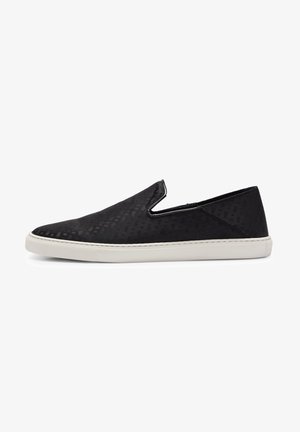 Baskets slip-on noires avec un motif texturé subtil et une semelle en caoutchouc blanche, vues de côté sur fond blanc.