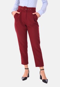 Pantaloni a vita alta bordeaux con una cintura ampia, tasche laterali e una vestibilità sartoriale. Abbinati a tacchi a punta neri per un look raffinato.