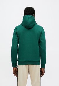 Zelená mikina s kapucňou z bavlneného zmesi, vybavená kapucňou, dlhými rukávmi a rebrovanými manžetami. Na zadnej strane je jednoduchý dizajn bez ozdôb.