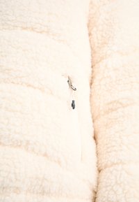 Fioletowy polar w kremowym kolorze z teksturowaną, puszystą powierzchnią. Posiada srebrny suwak z czarną linką i białą taśmą suwakową.