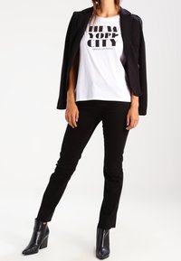 Blazer negro ajustado sobre una camiseta blanca con gráfico de "NEW YORK CITY", combinado con pantalones negros ajustados y botines.