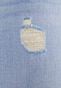 Ljusblå denimtyg med en framträdande ojämn reva med fransiga kanter, som blottar ett ljusare tyg under.