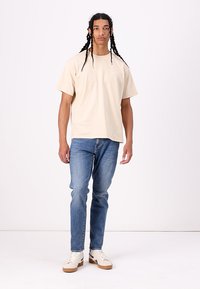 Tricou din bumbac bej cu mâneci scurte, asortat cu blugi din denim albastri. Pantofii sport au un design în nuanțe de alb și crem. Croială simplă, lejeră.