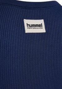 Granatowa dzianina prążkowana z białą prostokątną etykietą przyszytą przy dekolcie z napisem "hummel PERFORMANCE" czarnym drukiem.